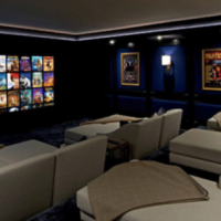 Cozy home theater with several light-colored reclining seats facing a wall-mounted screen of movie covers, dark blue walls, and framed posters.